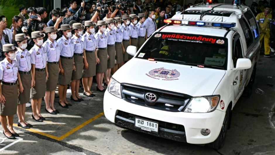 Thai police stand to attention as a convoy of ambulances leaves a Bangkok mortuary carrying the bodies of 23 people, most of them children, killed in a school bus fire