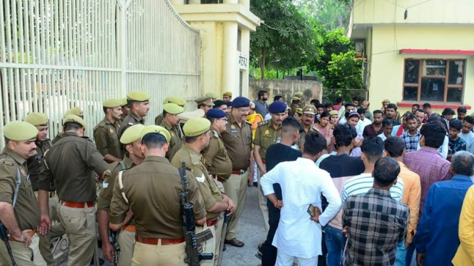 Policemen stand guard as mourners protest after newborns died in a hospital blaze in Jhansi 