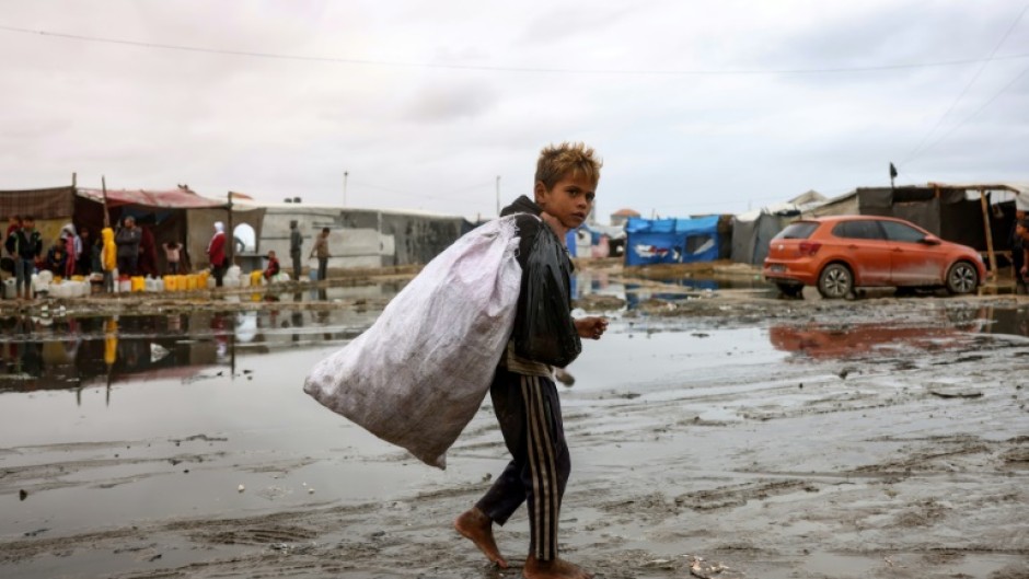 A displaced Palestinian child carrying a bag walks barefoot in a displacement camp in the central Gaza Strip 