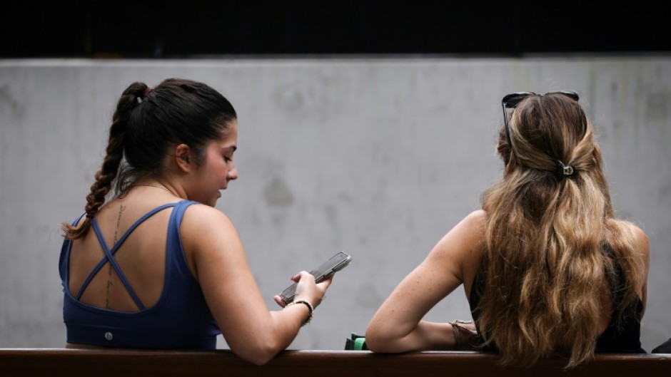 Two women sit on a bench looking at their phone in central Sydney. The Australian government says a new law aims to protect young people from the perils of social media