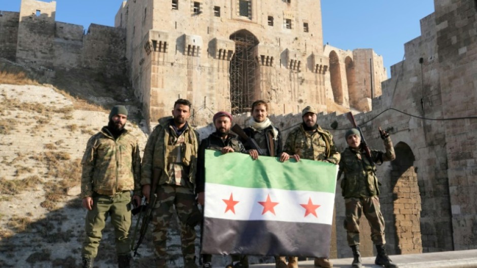 Anti-government fighters hold an opposition flag as they pose for a picture at the entrance of Aleppo's landmark citadel