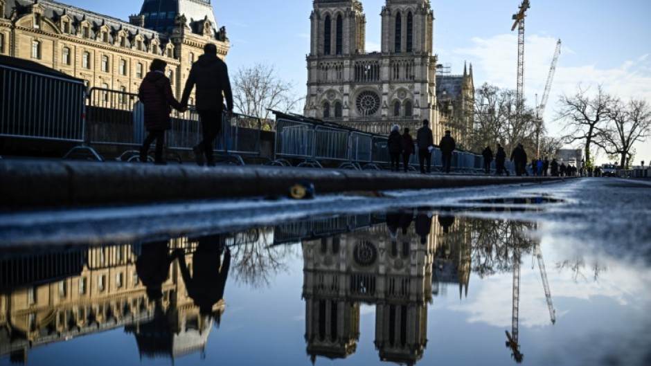 Pedestrians pass by the security barriers and fences placed around the Notre-Dame de Paris cathedral on the eve of its official reopening 