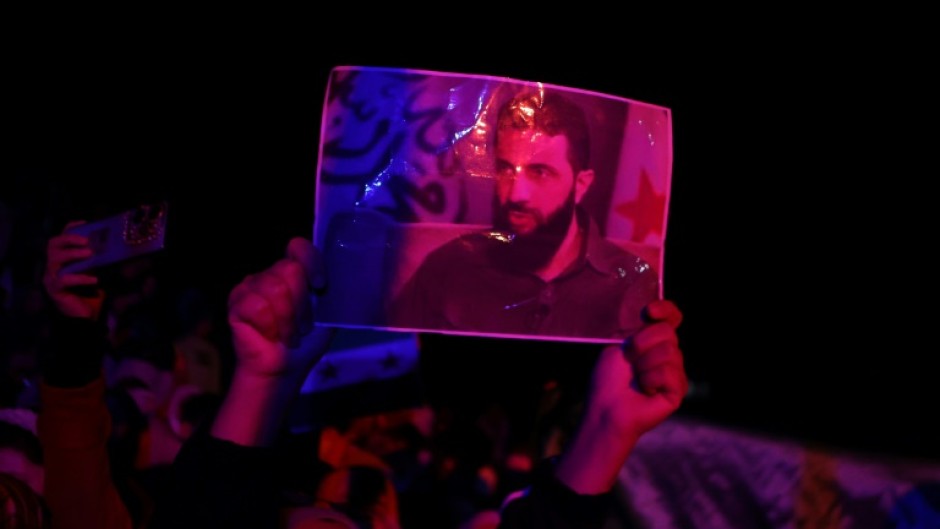 A woman lifts a picture of Islamist group Hayat Tahrir al-Sham (HTS) leader Abu Mohammed al-Jolani