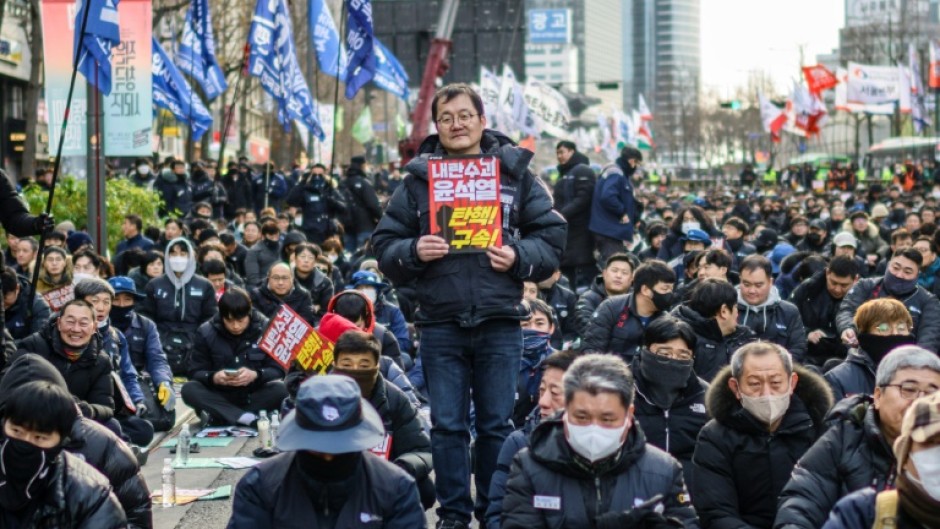 Kim Sung-tae (C), a 52-year-old worker at a company that makes car parts, poses with a placard reading "Insurrectionist Yoon Suk Yeol. Impeach! Arrest!"