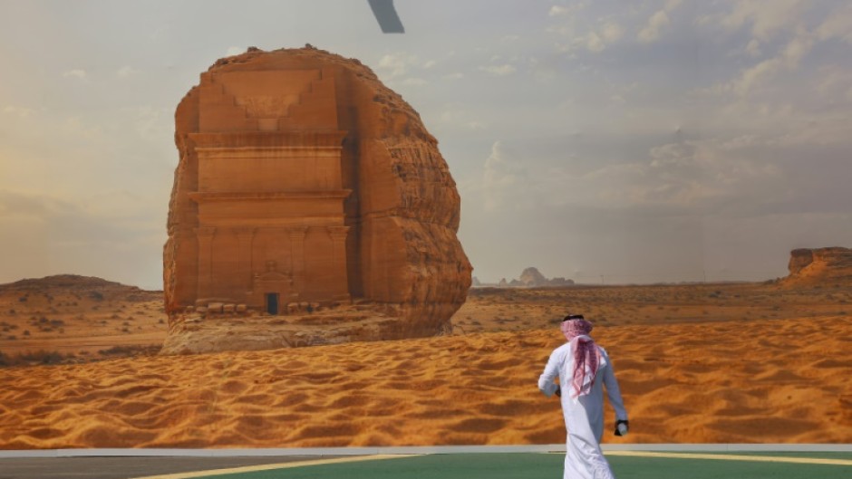 A COP16 delegate walks past a giant poster of a Saudi archaeological site at the start of the UNCCD talks