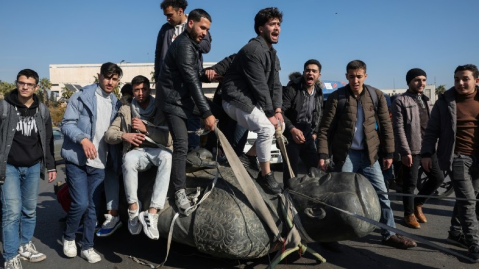 Damascus University students stand on a toppled statue of Syria's late president Hafez al-Assad during a rally near the campus