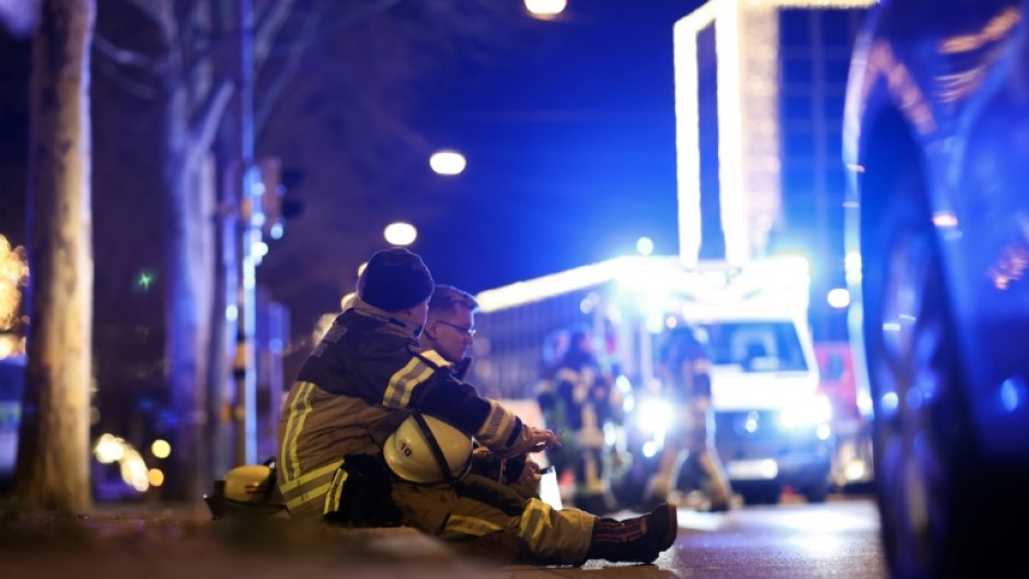 Two rescuers sit on the ground to rest after a car crashed into a crowd at a Christmas market injuring more than 60 people in Magdeburg, eastern Germany  
