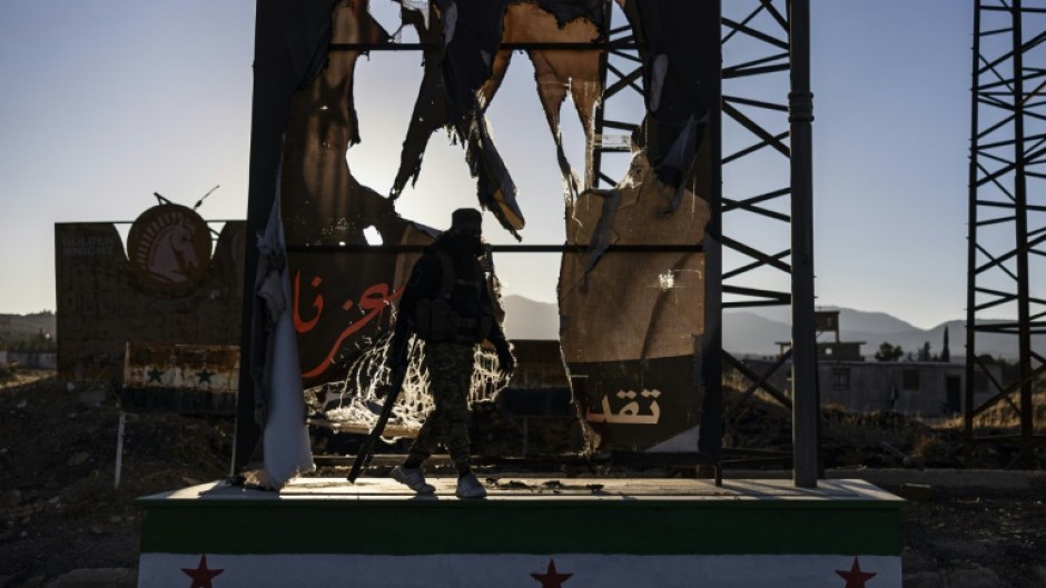 A rebel fighters walks past a defaced portrait of the toppled Syrian president Bashar al-Assad, in the town of Yafour near Damascus