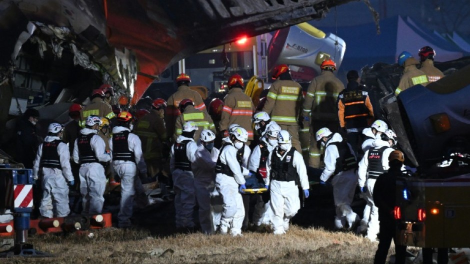 Firefighters and rescue personnel carry the body of a victim from the crash site