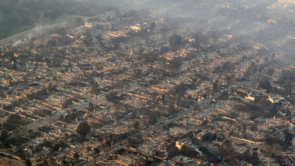 A man waters the front of his house as smoke and flames from the Palisades Fire burn toward the Encino neighborhood of Los Angeles, California