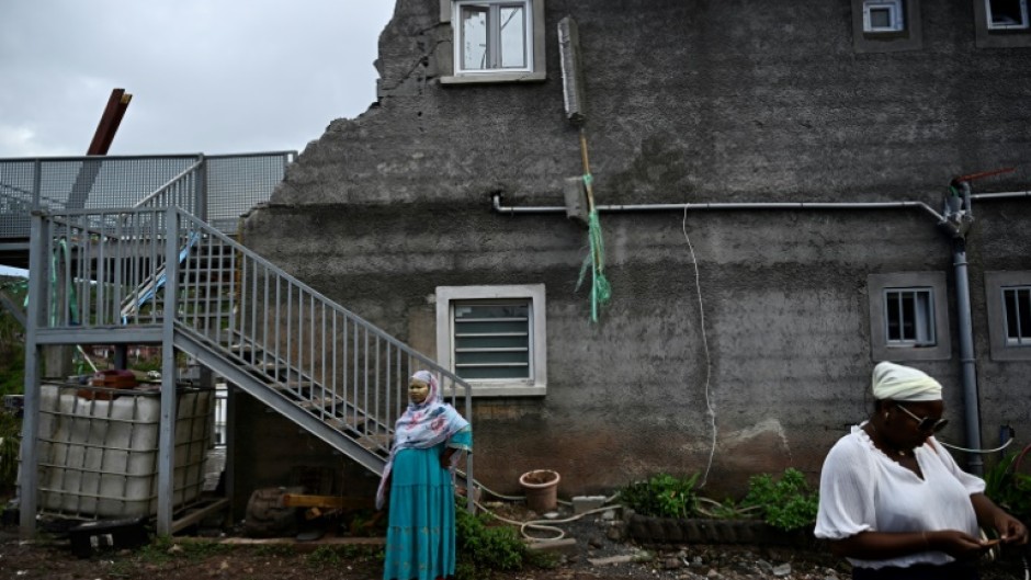 Local residents whose homes have been destroyed by the Chido cyclone stand in front of a damaged building in the village of Sohoa, on the French Indian Ocean territory of Mayotte