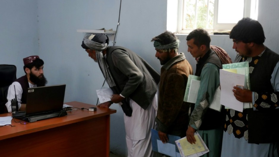 Afghan men stand in queue to submit their documents as they apply for passport in Herat