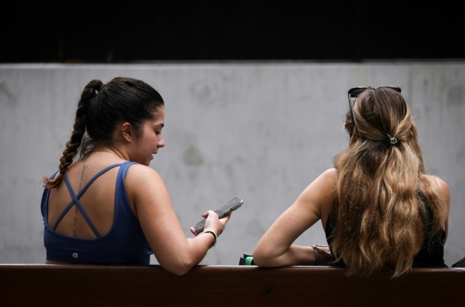 Two women sit on a bench looking at their phone in central Sydney. The Australian government says a new law aims to protect young people from the perils of social media