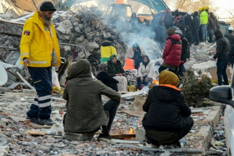 Victims' relatives sit around a fire next to the rubble of a collapsed building in Adiyaman