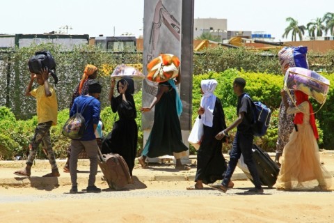 People carrying their belongings flee on foot along a street in southern Khartoum on April 18