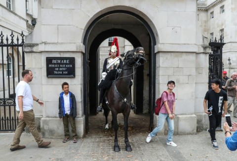 Tourists stand next to a member of The Life Guards squadron at Horse Guards in central London