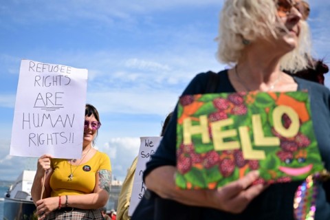 People hold up placards to welcome migrants to the barge which the government insists is a cost-effective option