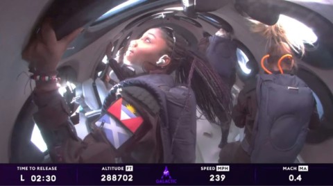 Anastatia Mayers (front L), Jon Goodwin (back R), and Chief Astronaut Instructor Beth Moses (front R) look out of windows in space aboard the Virgin Galactic spacecraft