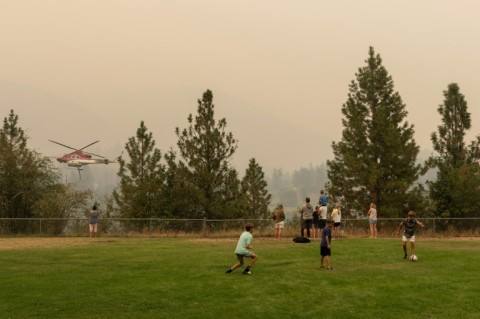 Families watch a helicopter fly by Shannon Lake to pick up water to battle wildfires outside West Kelowna, British Columbia