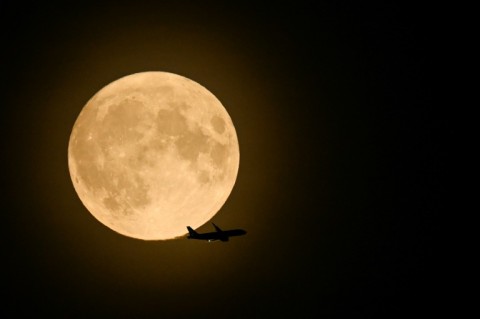 A British Airways Airbus A320 from Belfast and preparing to land at Heathrow, flies past the full moon rising in the skye of London, on August 30, 2023