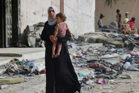 A Palestinian woman carries a child as she walks through debris in Gaza's residential neighbourhood of Rafah, following Israeli airstrikes on the southern Gaza Strip 