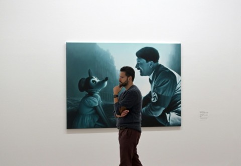 A visitor walks past a Helnwein painting called "Encounter 2 (The Man who Laughs)"  