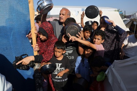 Palestinians who fled their houses amid Israeli strikes wait at a food distribution point as they shelter in tents set up by the United Nations in Gaza