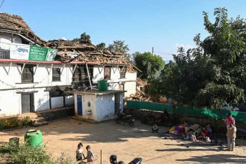 People rest outside next to a quake-damaged building in Jajarkot district