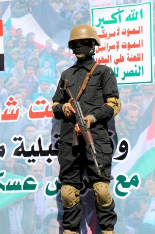 A Huthi fighter in front of a banner which reads in Arabic: 'Death to America, Death to Israel' 