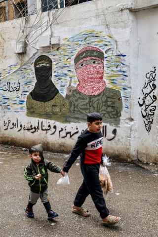 Children walk past a mural depicting fighters of the Qassam and Quds Brigades, the armed wings of the Palestinian Hamas and Islamic Jihad movements, painted on a wall in a camp for Palestinian refugees in Beirut's southern suburb 