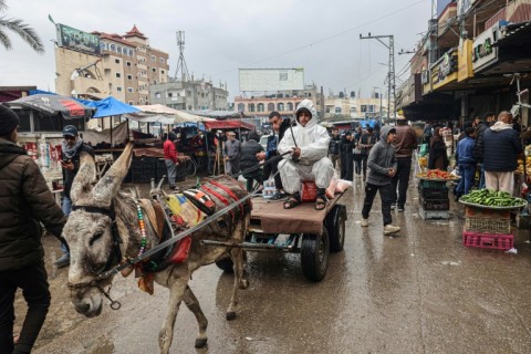 A man wearing a hazmat suit to keep warm, rides a donkey-pulled cart at a market in Rafah in the southern Gaza Strip on February 18, 2024