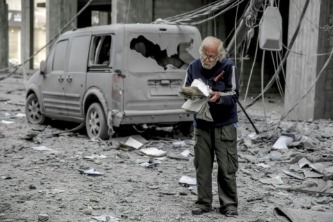 A Palestinian man reads a book in a Gaza City street damaged by Israeli bombardment 