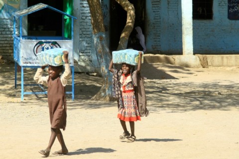 Sudanese children carry packs of relief supplies at a school outside Gedaref where their families have found refuge from the fighting