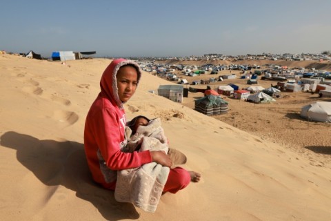 A Palestinian girl sits holding a toddler on a sand dune overlooking a camp for displaced people in Rafah in the southern Gaza Strip on March 17, 2024