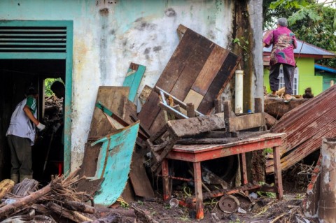 People clean a home that was damaged by mud and logs swept away by flash floods in western Indonesia