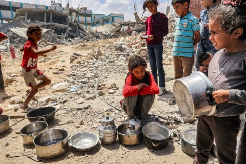 Children wait to receive food rations from an outdoor kitchen in Khan Yunis in the southern Gaza Strip 