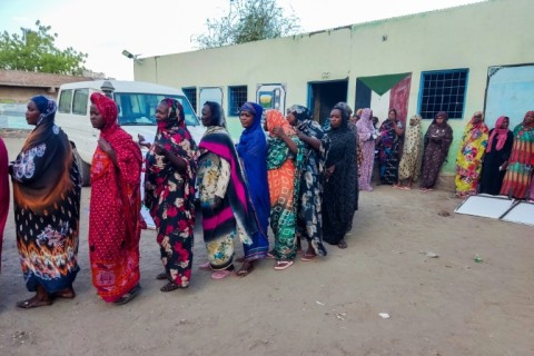 Internally displaced women wait in a queue to collect aid from a group at a camp in Gedaref