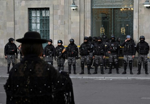 An indigenous Aymara woman walks in front of the government palace, guarded by riot police following a failed coup attempt