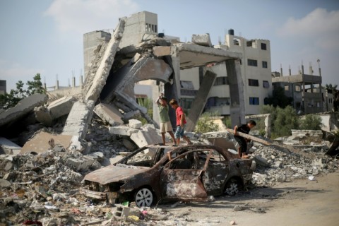 Palestinian children play on the wreckage of a car near a building destroyed in Israeli bombardment, in central Gaza's Al-Bureij refugee camp