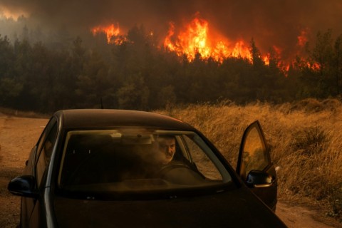 A man gets into his car to escape approaching flames as a wildfire blazes outside Athens