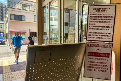 Customers walk by the entrance of a supermarket displaying signs warning of quake-related shortages