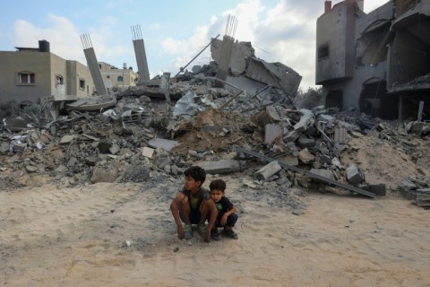 Children sit in front of a house targeted by an air strike in Nusseirat in the central Gaza Strip