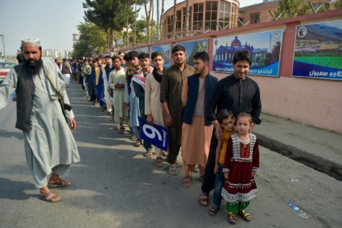 A Taliban security officer (L) is at work as Afghan cricket fans stand in line outside Kabul Cricket Stadium on August 22, 2024