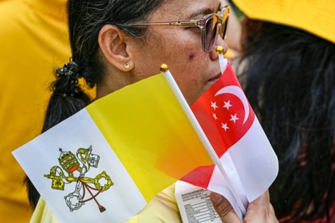 Catholic faithful with flags of Singapore and the Vatican wait for the arrival of Pope Francis at Changi Jurassic Mile in Singapore on September 11, 2024.