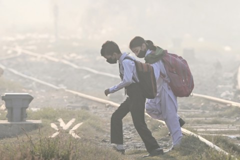 Schoolchildren wearing masks walk across a railway track amid thick smog in Lahore on Wednesday