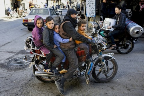 A man and his children ride on a motorcycle in Douma, east of the Syrian capital Damascus