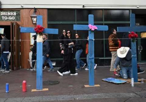 Tourists walk past as Eduardo Marquez paints crosses set up as a memorial near Bourbon Street, scene of a deadly truck-ramming attack