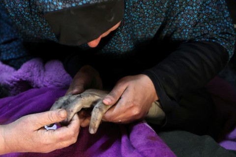 On New Year's Day, Palestinian women at Al-Ahli Arab Hospital in Gaza City mourn holding the hand of a relative killed in an Israeli strike 