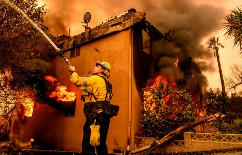 A firefighter douses flames as an apartment building burns during the Eaton fire in the Altadena area of Los Angeles county