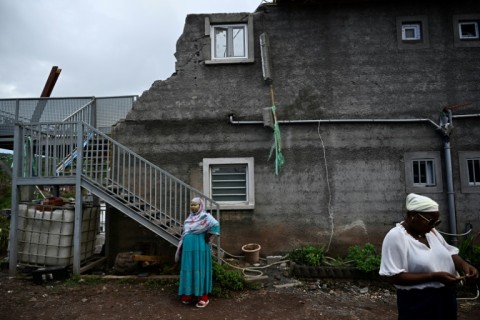 Local residents whose homes have been destroyed by the Chido cyclone stand in front of a damaged building in the village of Sohoa, on the French Indian Ocean territory of Mayotte